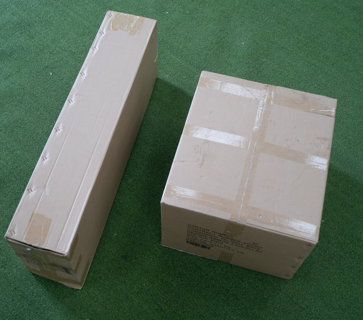 SimBox Golf Simulator Enclosure packed in two taped cardboard shipping boxes, one long narrow carton and one square box